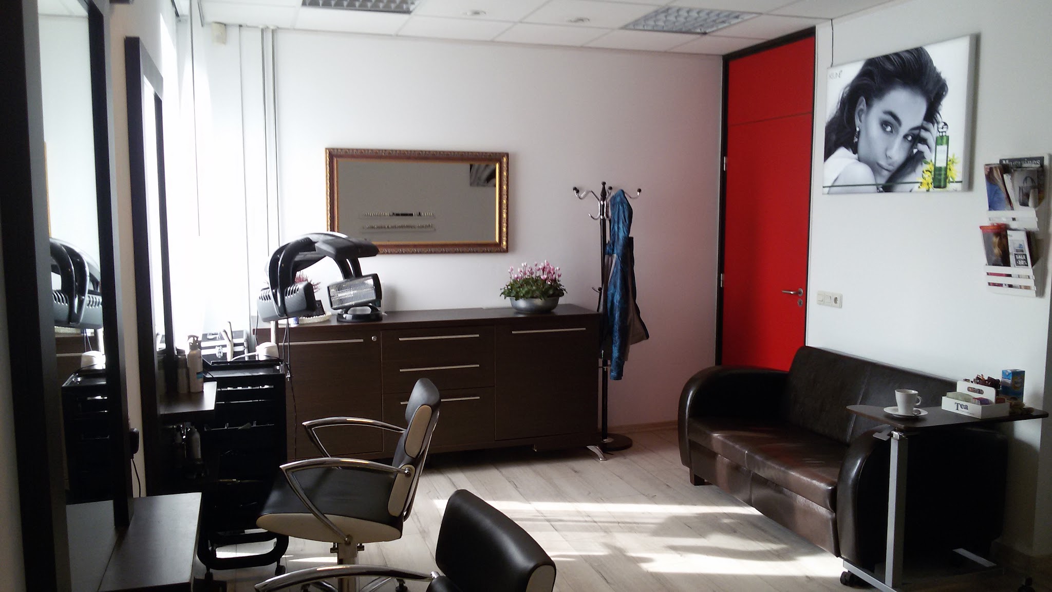 Een kapstoel voor de spiegel, een bruine bank en de rode deur, met een zwart-witportret aan de wand