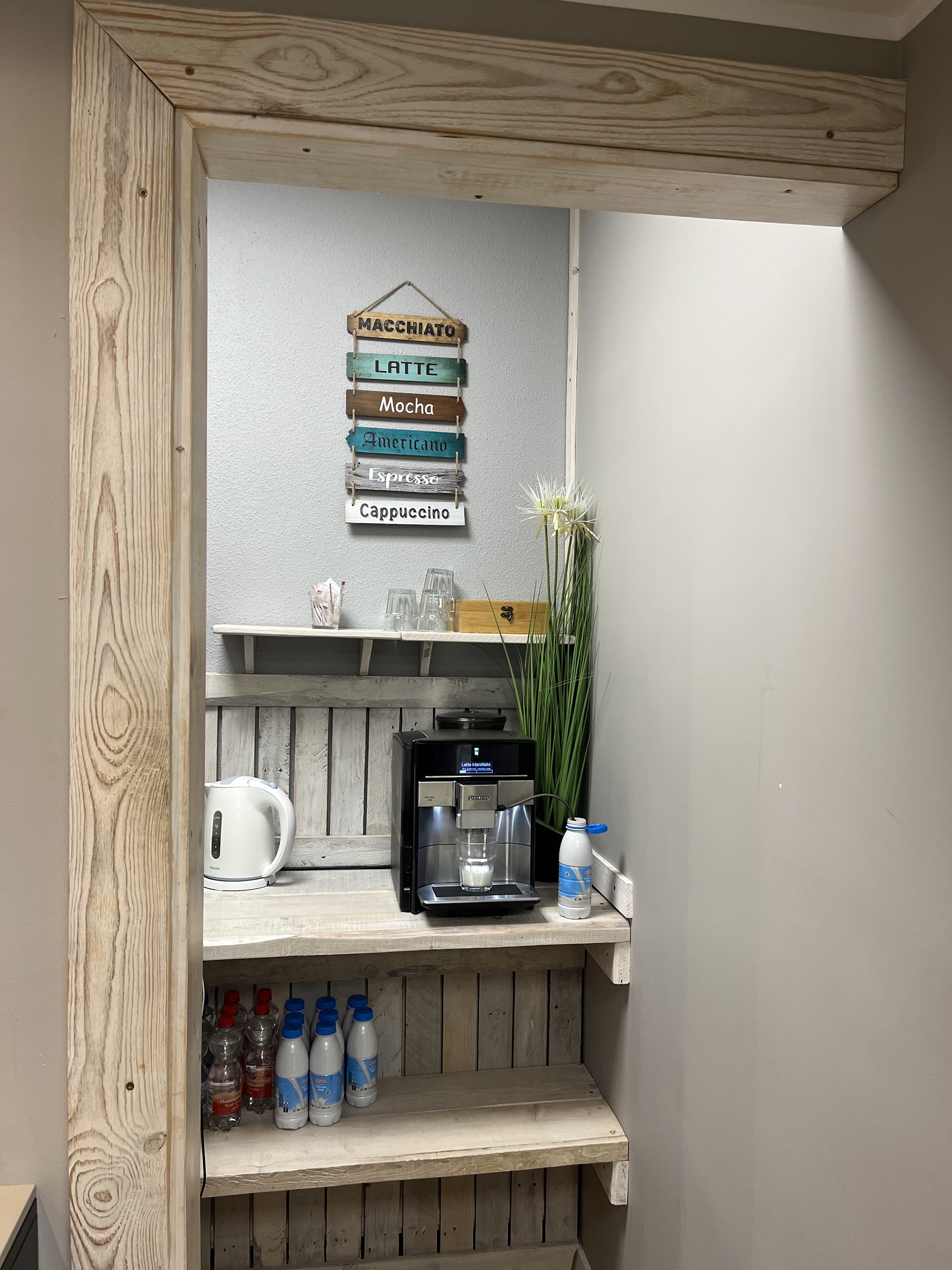 De koffiehoek in een houten lijst, met een koffiemachine en een bordje met koffiesoorten